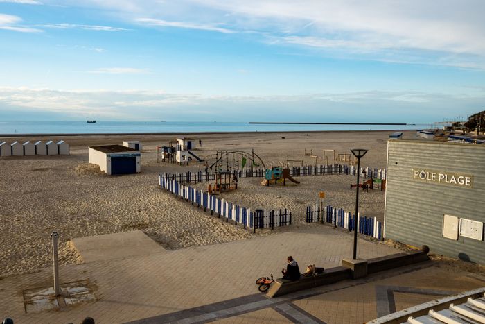 A serene beach scene at Boulogne-sur-Mer with a playground and beach huts under a clear sky.