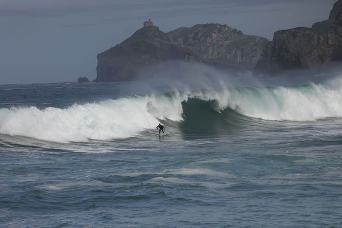 Exciting scene of a surfer tackling massive waves near a rocky coastline under a clear sky.