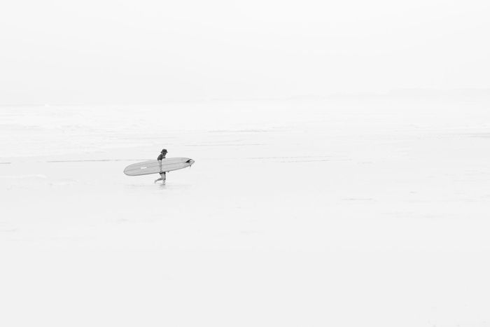A solitary surfer walks along the serene Takanabe Beach, Japan, carrying a surfboard.