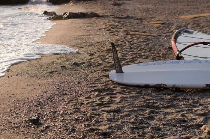 Surfboard lying on a serene Greek beach shore during a sunny morning, capturing the essence of a quiet vacation spot.