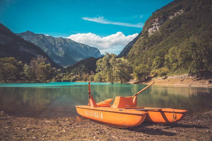 Orange pedal boat by a serene lake surrounded by mountains in Trentino-South Tyrol, Italy.