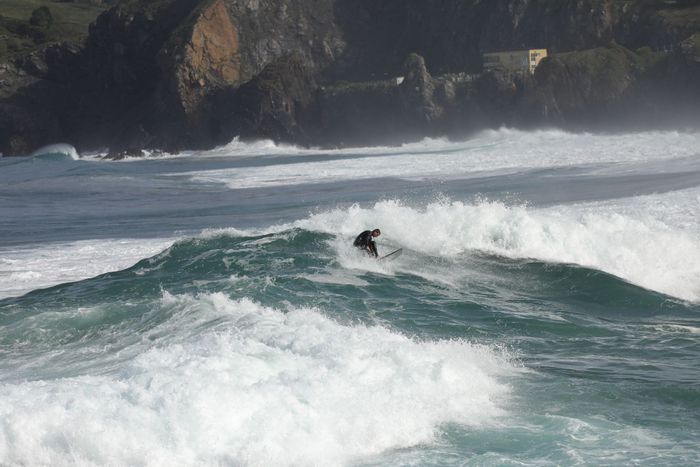 A surfer rides powerful ocean waves on a sunny day in Bakio, Bizkaia, capturing the essence of surf culture.