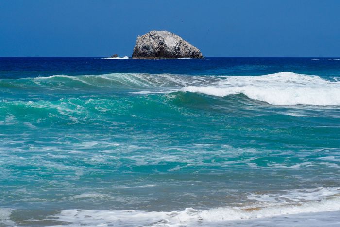 Vibrant ocean waves and rock formation off the coast of Oaxaca, Mexico.