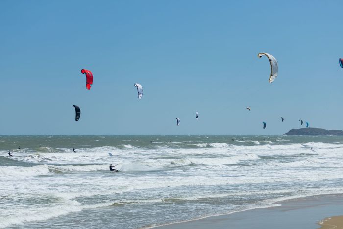 Kitesurfers enjoy a sunny day at the beach, riding the waves and soaring in the breeze.