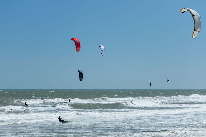 Kitesurfers enjoy thrilling action over the ocean waves under a clear blue sky.