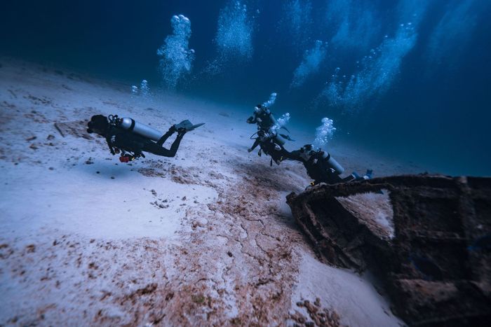 Scuba divers explore a shipwreck in Isla Mujeres, Mexico, amidst bubbles and sea life.
