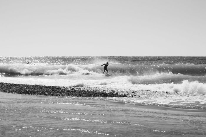 Black and white photo of a surfer riding waves on a pebbled beach in Sochi, Russia.