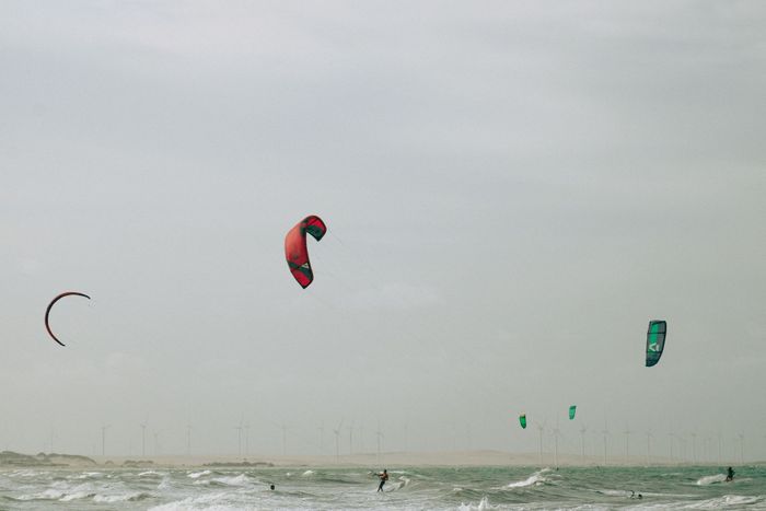Kitesurfers enjoy thrilling rides on the ocean waves with wind turbines in the distance, a blend of adventure and renewable energy.