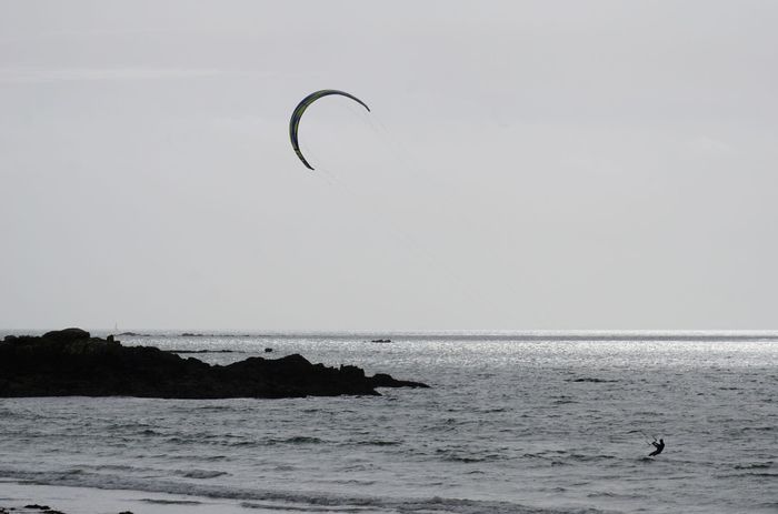 A kitesurfer glides across the sea near rocky shores, capturing a thrilling oceanic sport.