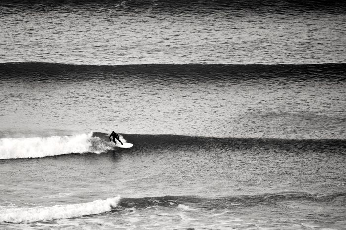 Monochrome photograph of a surfer riding waves in the ocean, taken in England, UK.