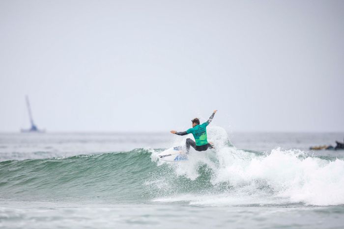 Professional surfer performing an aerial maneuver on a wave during a competition.