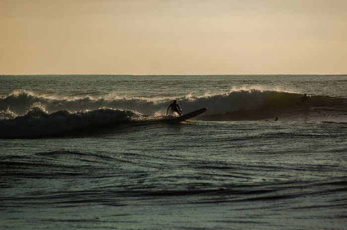 A surfer skillfully rides a wave during a picturesque sunset on the coast of Bretagne, France.