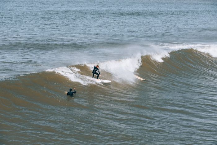 Surfer riding waves with a fellow surfer nearby, capturing the thrill of ocean surfing.