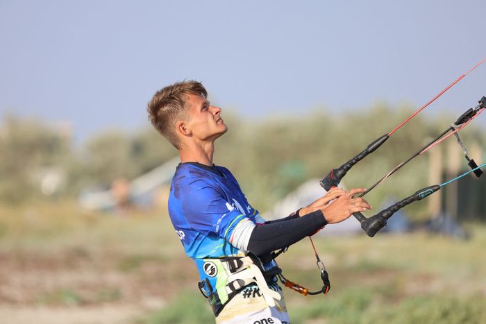 Portrait of a young man kitesurfing outdoors, focused and looking up, wearing a blue shirt and harness.