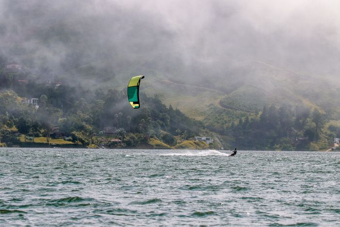Experience thrilling kitesurfing in a misty bay with lush green hills as the backdrop.
