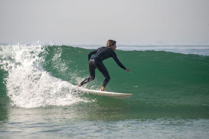 Dynamic surfer in wetsuit skillfully rides a wave at Portugal. Perfect for summer sports themes.