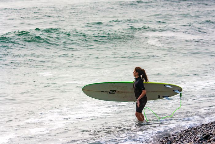 A woman holds her surfboard while walking by the sea in Lima, Peru.