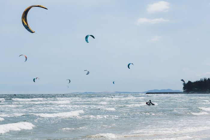 A dynamic scene of kitesurfers riding waves along a sunny coastal shore with clear skies.