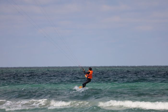 A kitesurfer in an orange vest enjoying a thrilling ride on the ocean waves under a clear sky.