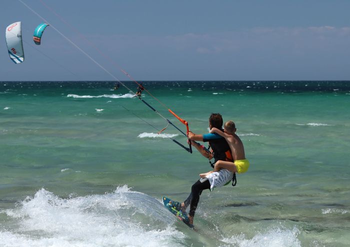 Dynamic scene of father and son kitesurfing together on a sunny day at the beach.