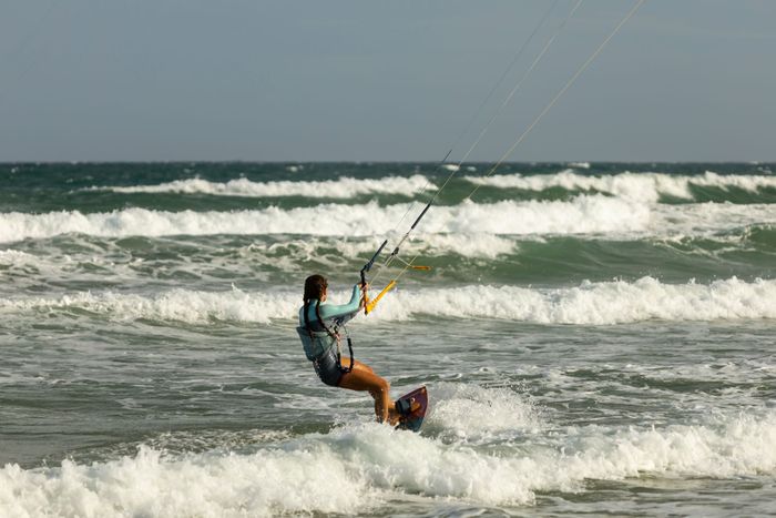A woman skillfully kite surfing along waves on a bright, sunny beach day.