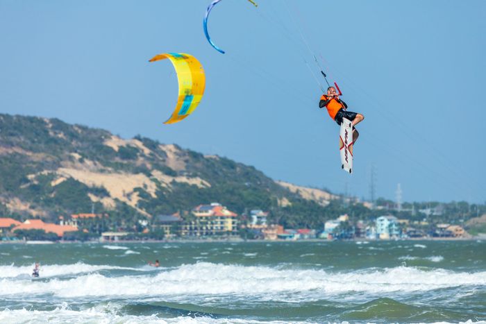 Dynamic kitesurfing scene with a man soaring above ocean waves on a sunny day, showcasing adventure and excitement.