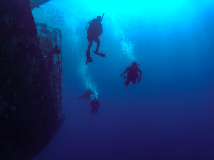 A group of scuba divers exploring a submerged shipwreck in the deep blue waters of Saudi Arabia.