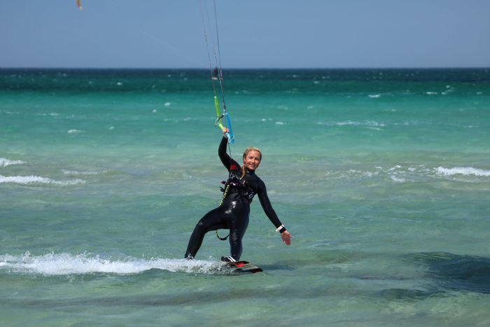 A woman in a wetsuit kiteboarding on turquoise ocean waters on a bright day.
