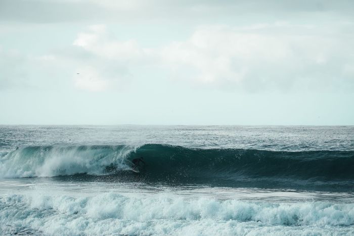 A surfer glides through a breaking wave in Punta del Este, Uruguay, against a cloudy sky.