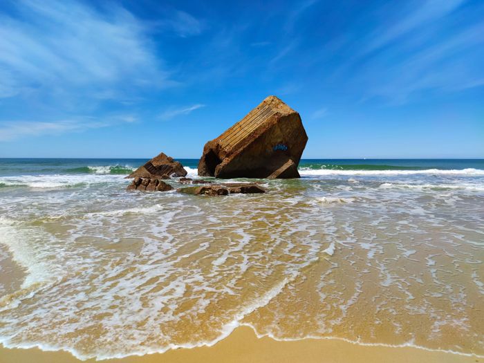 A scenic view of an old bunker on Capbreton beach with clear skies and ocean waves.