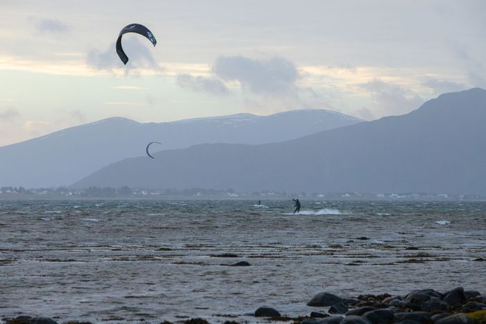 Dynamic image of kiteboarders against scenic mountains at Giske, Norway's coastline.