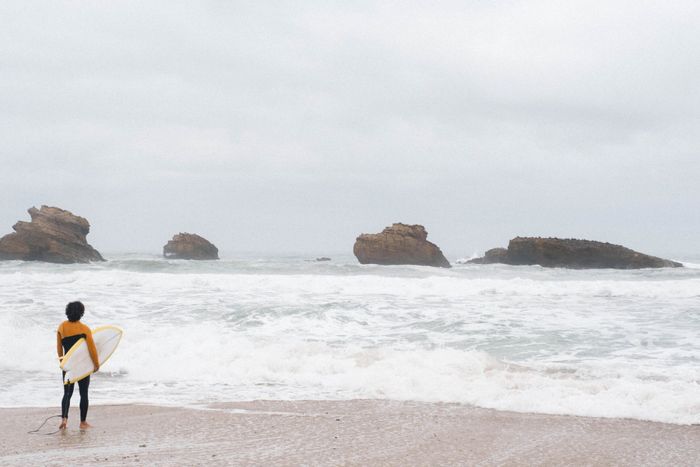 Surfer preparing to enter the ocean on a cloudy day at Biarritz beach, France.