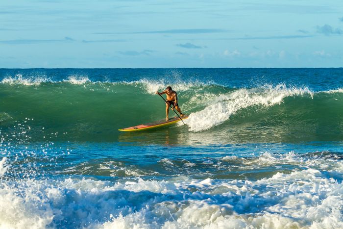 Dynamic action shot of a man paddleboarding on powerful ocean waves on a sunny day.