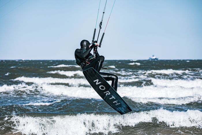A kitesurfer in a wetsuit rides ocean waves with high energy and style.
