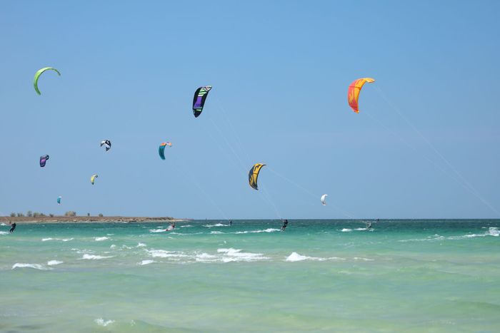 Experience thrill and freedom with kiteboarders gliding across the sea under a bright blue sky.