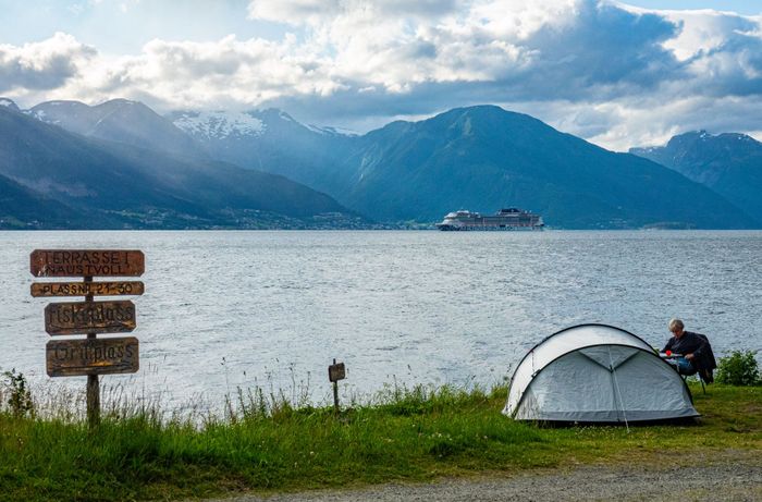 Scenic view of tent by a fjord in Norway, with cruise ship and mountains.