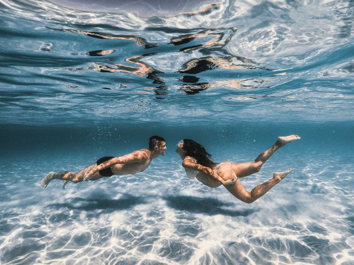 A couple swims face to face underwater in clear blue waters, showcasing a serene and romantic moment in a tropical sea.