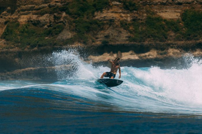 Shirtless surfer riding powerful waves in beautiful Indonesian seascape.