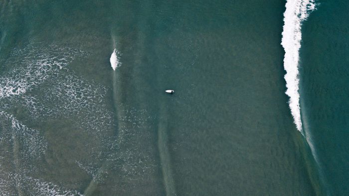 Drone shot capturing a lone surfer navigating ocean waves, perfect for beach sports themes.
