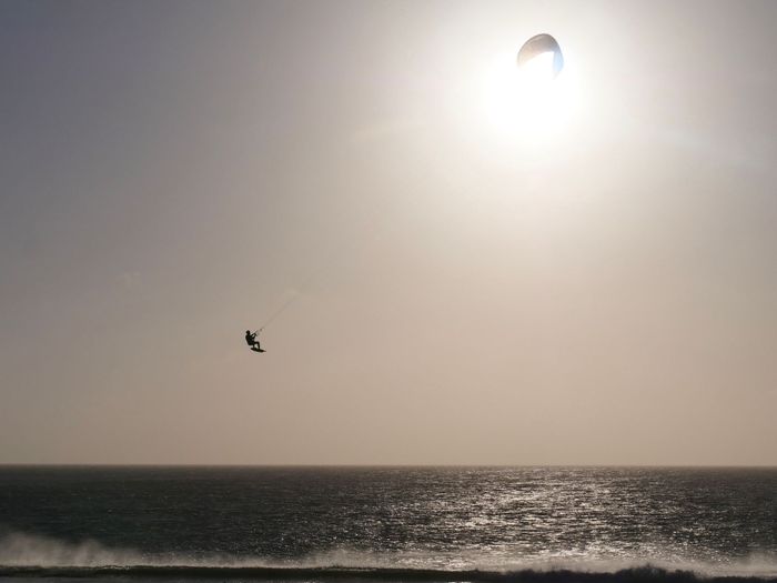 A kitesurfer catching air over the sea beneath a bright sun in Tarifa, Spain.