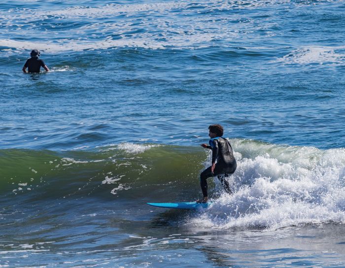 A surfer skillfully rides a wave at the beach, showcasing water sports excitement.