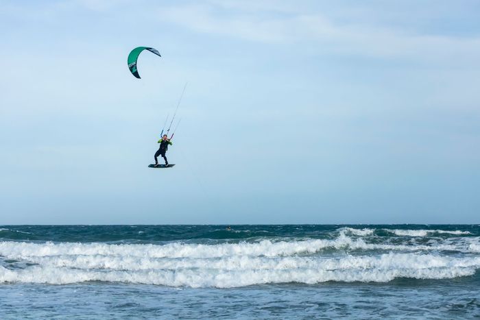 A kitesurfer catches air above the ocean waves, showcasing thrilling water sport action.