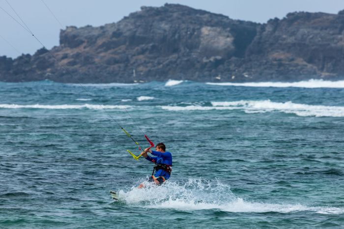 A thrilling kiteboarding adventure in a vibrant turquoise sea with rocky cliffs in the background.