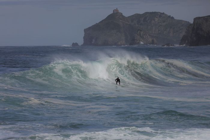 Dynamic scene of a surfer catching waves against dramatic cliffs at Bakio, Basque Country.