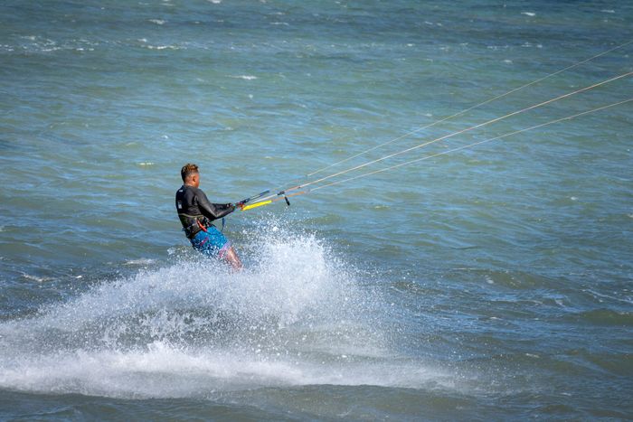 Side view of unrecognizable sportsman in wetsuit splashing sea water while practicing wakeskating during summer vacation