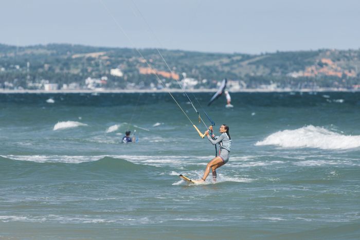Woman enjoying kitesurfing on a sunny coastal beach with waves.
