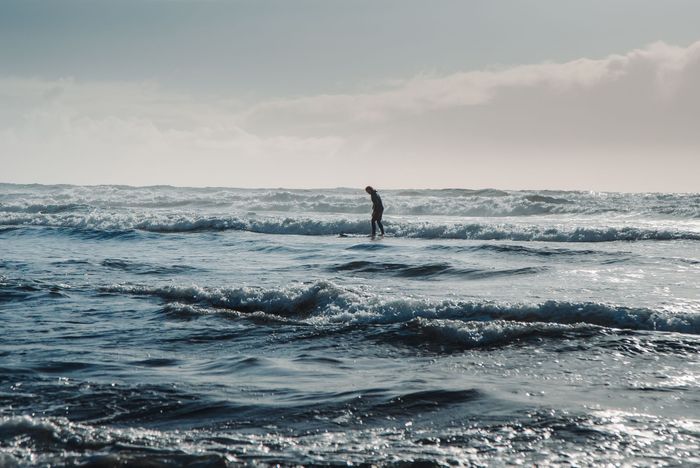 A surfer skillfully rides waves under a clear blue sky on Oregon's scenic coastline.