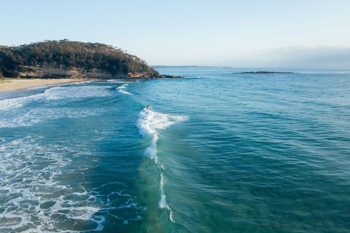 A stunning aerial shot of Narrawallee Beach in NSW, Australia, with crashing waves and lush green coastline.