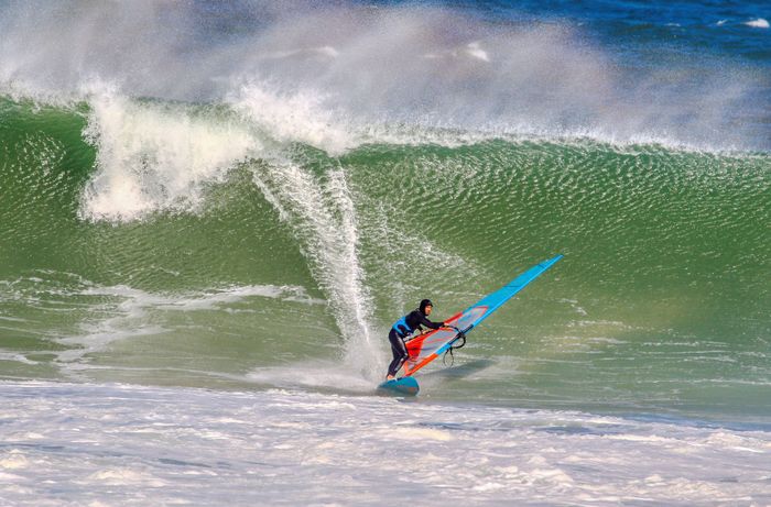 A dynamic image capturing a windsurfer riding a large ocean wave, showcasing the thrill of the sport.