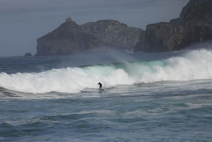 A lone surfer rides a wave against stunning coastal cliffs at Bakio Beach, Basque Country.
